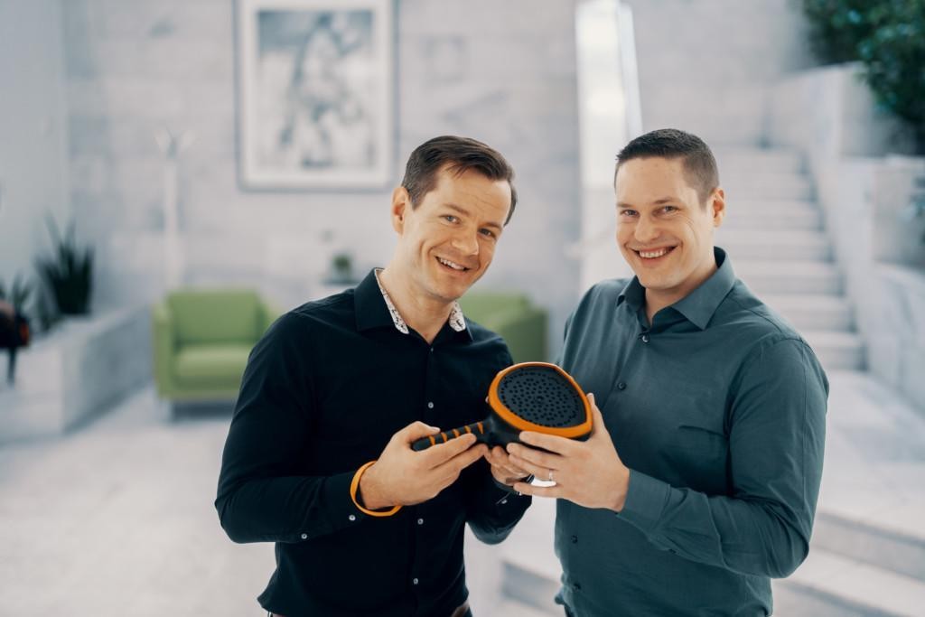 Two men standing side by side and holding an acoustic camera in their hands together.